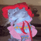 a cat wearing a pink sweater and a red hat is sticking its tongue out