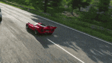 a red sports car is driving down a road with trees in the background