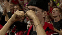 a man wearing glasses and a beanie wipes his eyes while watching a game