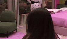 a woman is standing in a room with a bed and a chair
