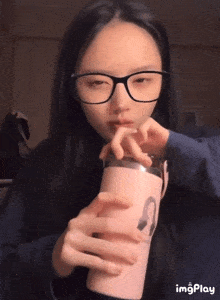 a girl wearing glasses is drinking from a pink tumbler