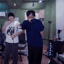 a man in a blue sweater is singing into a microphone next to a man in a white shirt that says " black "