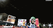 a man wearing a green helmet and goggles is screaming in front of a sign that says akon.de