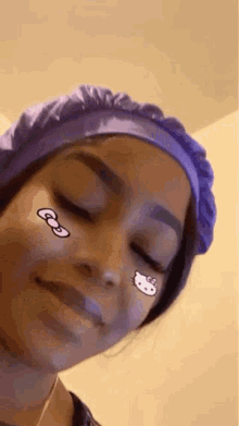 a woman wearing a purple hat and a hello kitty sticker on her face is smiling .
