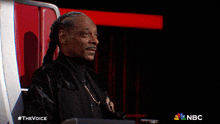 snoop dogg is sitting in a chair with his hand on his forehead and a nbc logo behind him