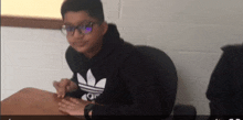 a boy wearing a black adidas sweatshirt sits at a table