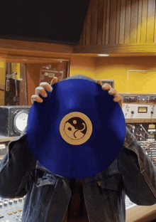 a person covering their face with a blue record with a yin yang symbol on it