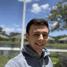 a young man in a gray hoodie is smiling for a selfie .
