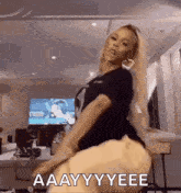 a woman is dancing in a living room in front of a television while wearing a black shirt and heart shaped earrings .