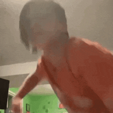 a man in a red shirt is dancing in a room with a green wall .
