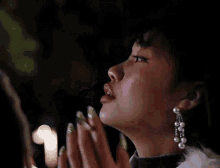 a woman with green nails and pearl earrings is eating a slice of lime .