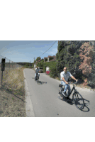 two men are riding bicycles down a road in front of a sign that says " no parking "