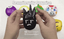 a person is holding a black object with a face on it and the words " sempiternity surprise " written above it