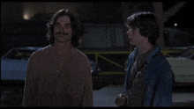 two men are standing next to each other in a parking lot at night