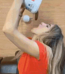 a woman in an orange shirt is drinking from a bottle of milk