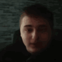 a close up of a man 's face in a dark room with a brick wall in the background .