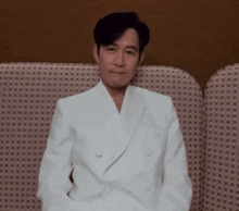 a man in a white suit sits on a couch with his hands in his pockets
