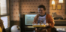 a man in a flames shirt is holding a tray of food in front of a netflix sign