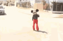 a person in a mickey mouse costume is dancing on the sidewalk .