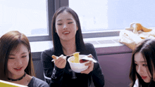 a woman holding a bowl of noodles with chopsticks is smiling