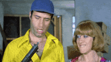 a man in a blue hat holds a gun next to a woman in a wig