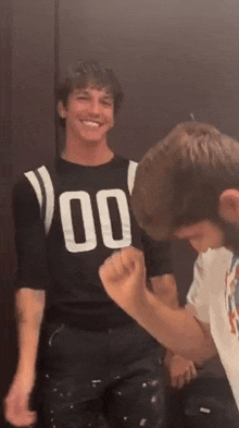 a man in a black shirt with the number 00 on it is standing next to another man in a white shirt .