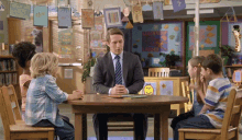 a man in a suit sits at a table with children