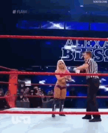 a woman is standing in a wrestling ring with a referee and a sign that says alexa bliss