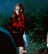 a woman in a red sweater and black shorts stands in a dark forest and says " fact "