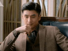 a man in a suit and tie is sitting in a chair with his hand on his chin