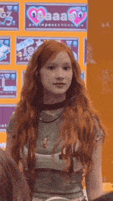 a girl with red hair is standing in front of a wall with a heart shaped sign that says aaa on it