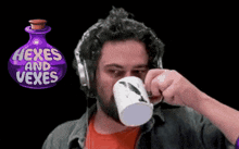 a man drinking from a mug with a bottle of hexes and vexes behind him