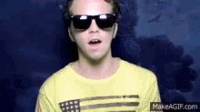 a man wearing sunglasses and a yellow shirt with an american flag on it is making a funny face .