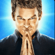 a man with his hands folded in prayer looks at the camera