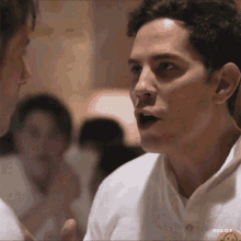 a man wearing a white shirt with a smiley face on it talking to another man