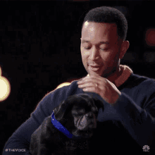 a man is petting a small black dog with a blue collar .