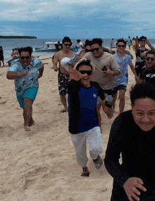 a group of people are running on a beach and one of them is wearing a blue shirt with a bird on it