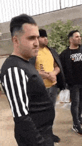 a group of men are standing next to each other on a sidewalk . one of the men is wearing a yellow shirt .