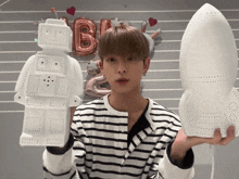 a boy in a striped shirt is holding a robot and a rocket in his hands