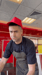 a man wearing a red hat and an apron is standing in front of a red wall