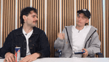 two men are sitting at a table with a red bull can in front of them