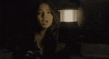 a woman is holding a lantern in the dark and looking at the camera .