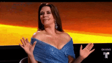 a woman in a blue dress is sitting in a chair with her hands outstretched .