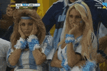 two women are watching a soccer game and the score is 1-0