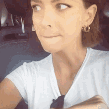 a woman wearing hoop earrings and a white shirt looks at the camera
