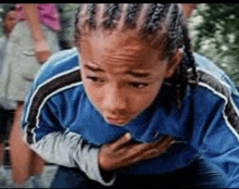 a young boy with braids is holding his chest and looking down .