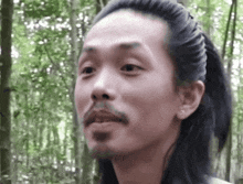 a man with a ponytail and a beard looks at the camera