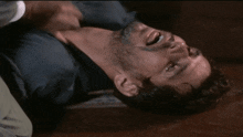 a man in a blue shirt is laying on the floor with his hand on his neck