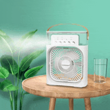 a white fan is sitting on a wooden table next to a glass of water .