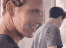 a man is smiling and looking at the camera while another man is standing behind him .